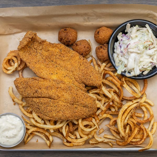 Fried fish fillets, hush puppies, curly fries, coleslaw, and tartar sauce on a tray.