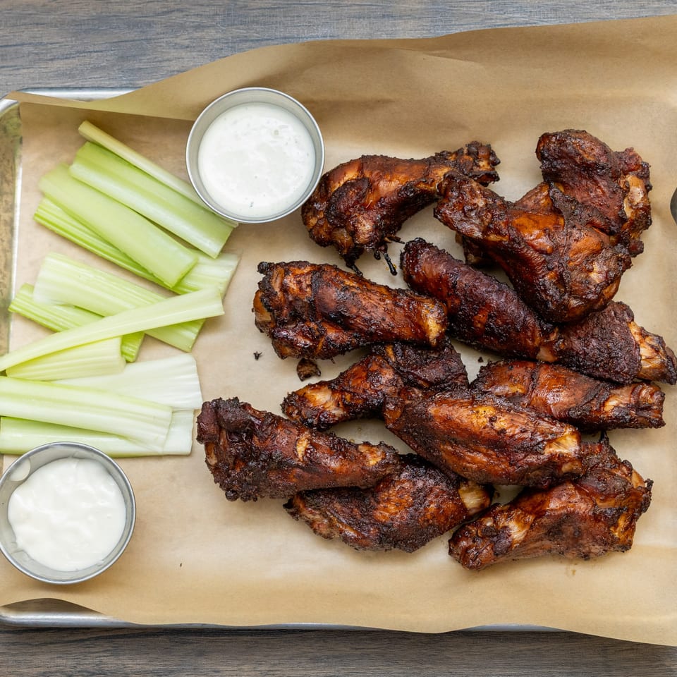 A tray of dark, crispy chicken wings with celery sticks and two small cups of ranch dressing.