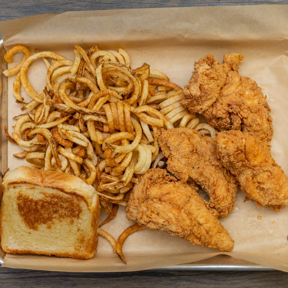 Crispy fried chicken tenders, curly fries, and a slice of Texas toast on a metal tray.