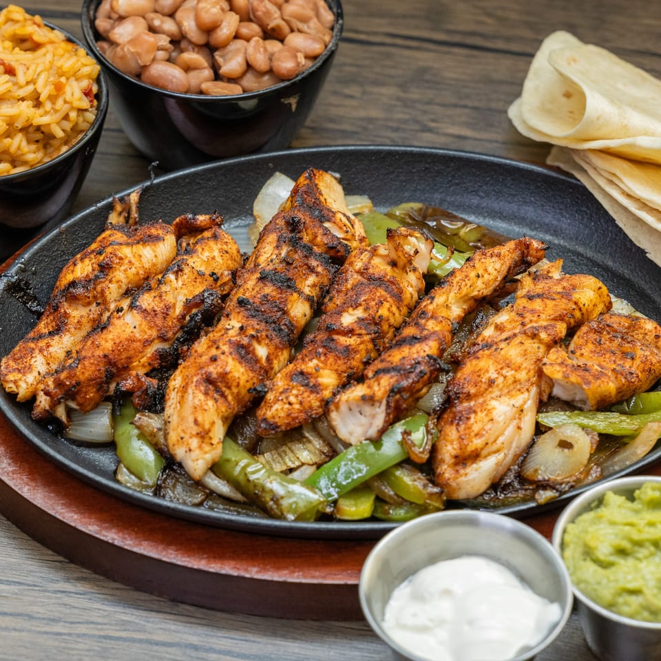 Sizzling chicken fajitas with grilled peppers and onions, served with rice, beans, tortillas, guacamole, and sour cream.